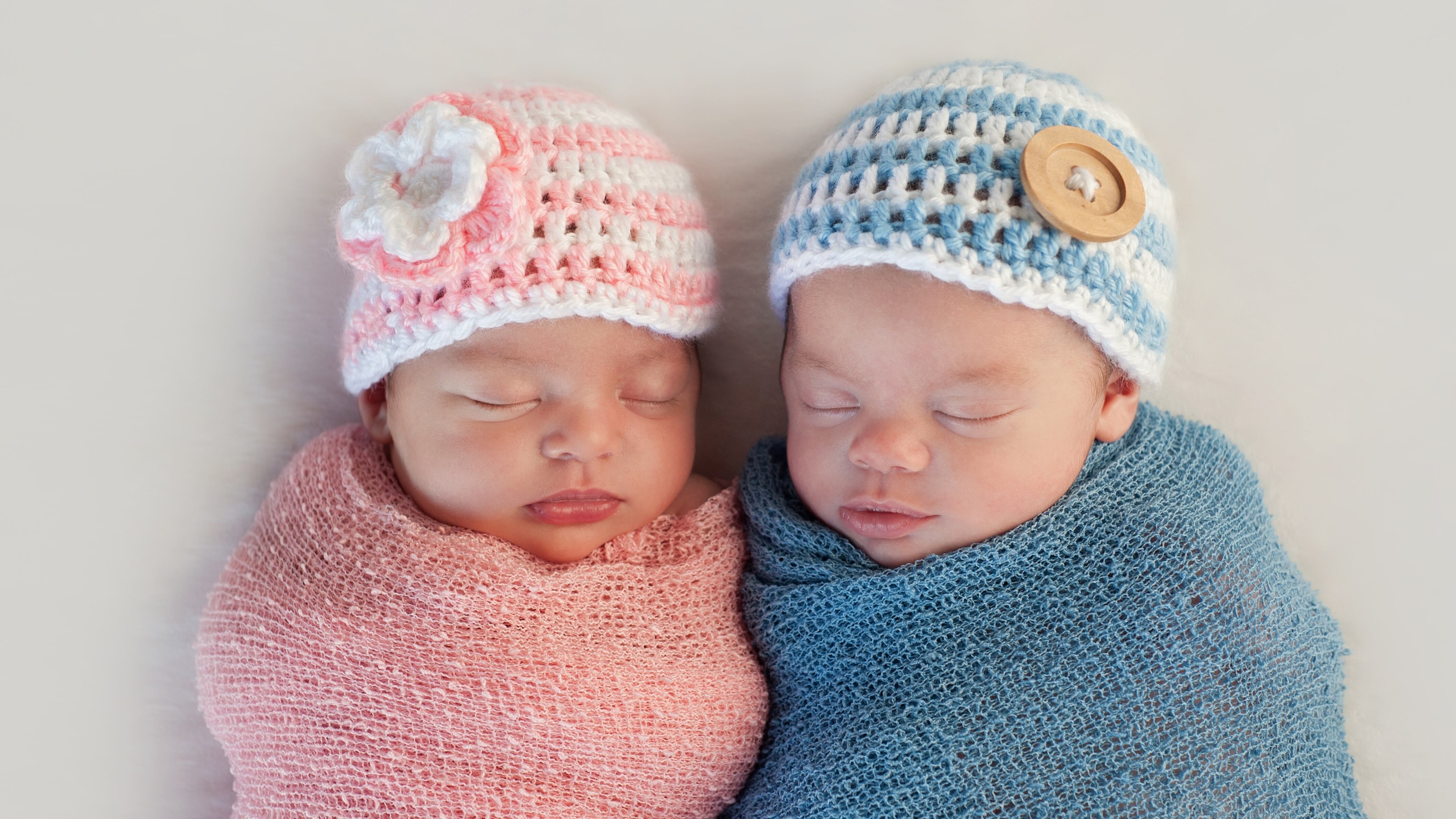 Five week old sleeping boy and girl fraternal twin newborn babies. They are wearing crocheted pink and blue striped hats.